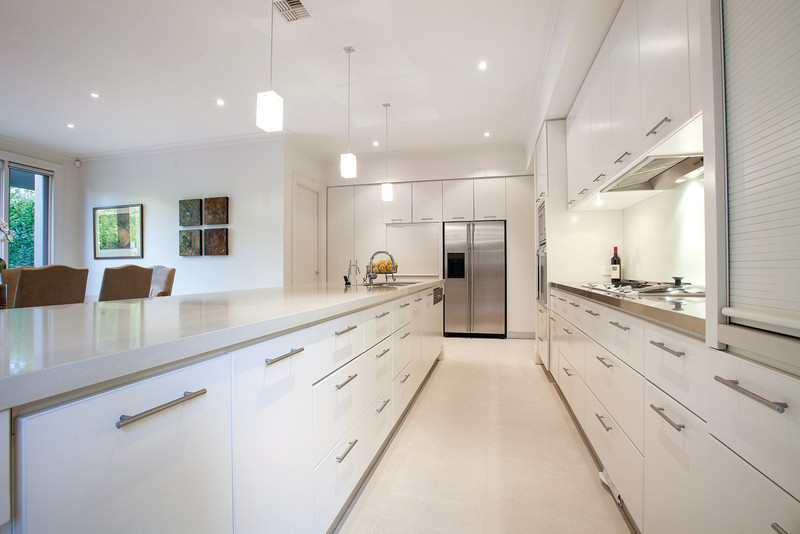 Photo of a large traditional galley eat-in kitchen in Melbourne with an undermount sink, flat-panel cabinets, white cabinets, quartz benchtops, white splashback, glass sheet splashback, stainless steel appliances, ceramic floors and with island.