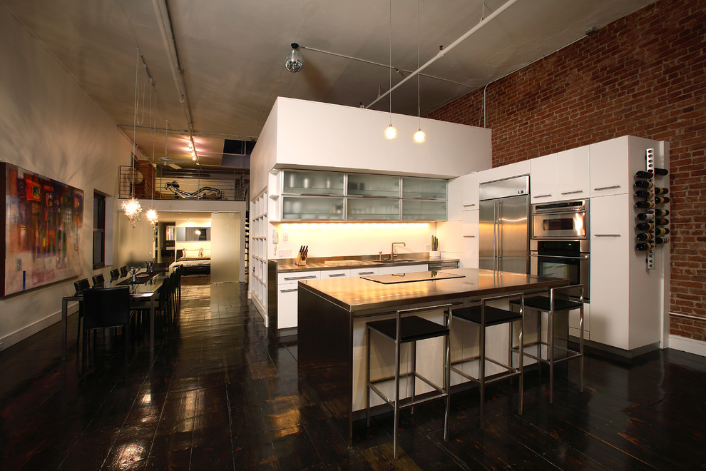 This is an example of a contemporary l-shaped eat-in kitchen in New York with stainless steel benchtops, flat-panel cabinets, white cabinets, stainless steel appliances, linoleum floors and with island.