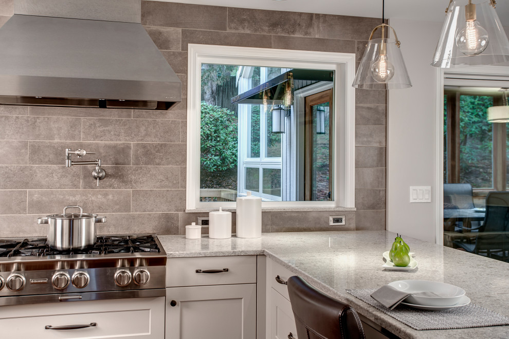 This is an example of a large transitional l-shaped eat-in kitchen in Seattle with an undermount sink, recessed-panel cabinets, white cabinets, quartz benchtops, grey splashback, porcelain splashback, stainless steel appliances, medium hardwood floors, red floor and grey benchtop.
