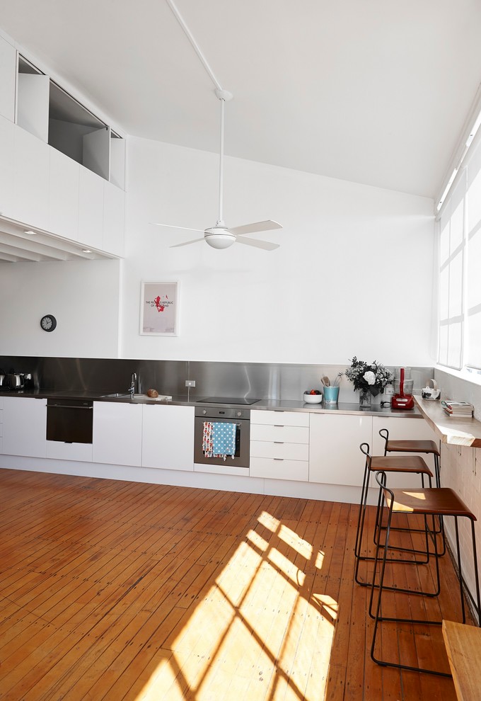 This is an example of a mid-sized contemporary single-wall eat-in kitchen in Auckland with a double-bowl sink, white cabinets, stainless steel benchtops, grey splashback, stainless steel appliances, no island, medium hardwood floors and grey benchtop.