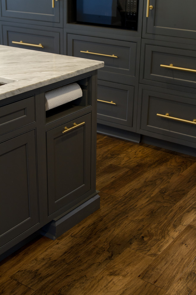 Example of a transitional medium tone wood floor and brown floor eat-in kitchen design with beaded inset cabinets, gray cabinets, white backsplash, paneled appliances, an island and white countertops