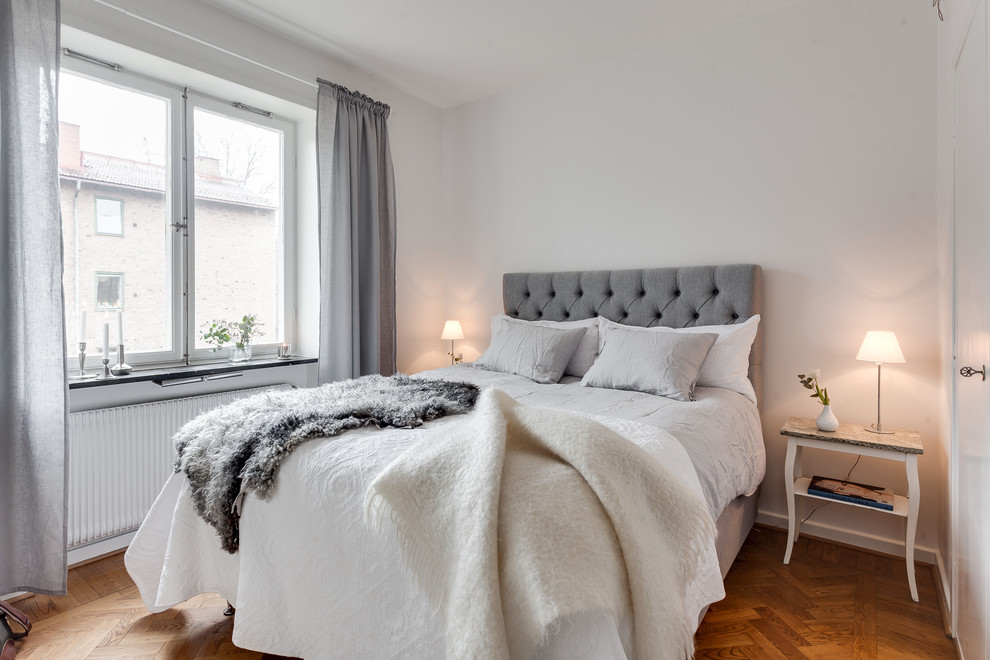 This is an example of a mid-sized scandinavian master bedroom in Stockholm with white walls, medium hardwood floors and no fireplace.