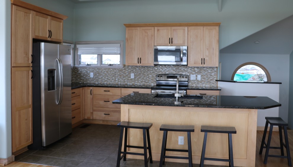 Photo of a mid-sized beach style l-shaped eat-in kitchen in Raleigh with an undermount sink, shaker cabinets, light wood cabinets, granite benchtops, multi-coloured splashback, stainless steel appliances, ceramic floors, with island, glass tile splashback and black benchtop.