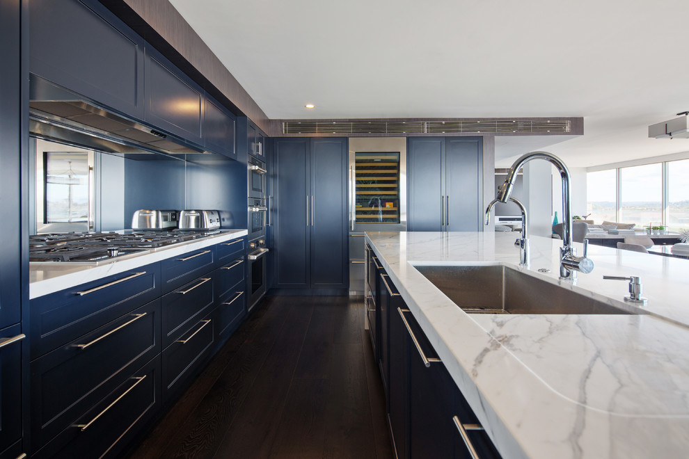 Photo of a large contemporary galley open plan kitchen in Sydney with an undermount sink, shaker cabinets, blue cabinets, marble benchtops, mirror splashback, stainless steel appliances, dark hardwood floors, with island and black floor.