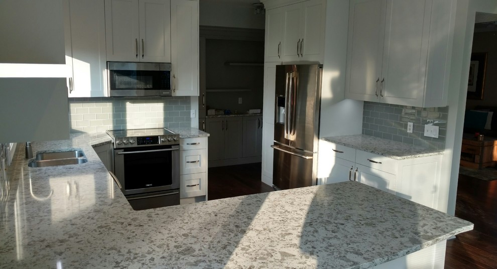 Example of a mid-sized transitional u-shaped eat-in kitchen design with an undermount sink, flat-panel cabinets, white cabinets, quartz countertops, gray backsplash, glass tile backsplash and stainless steel appliances