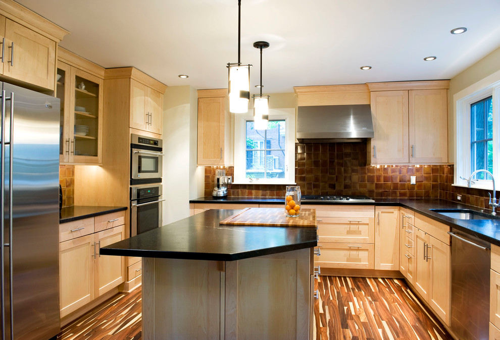 Example of a mid-sized trendy u-shaped medium tone wood floor eat-in kitchen design in Baltimore with soapstone countertops, a drop-in sink, recessed-panel cabinets, light wood cabinets, brown backsplash, ceramic backsplash, stainless steel appliances and an island