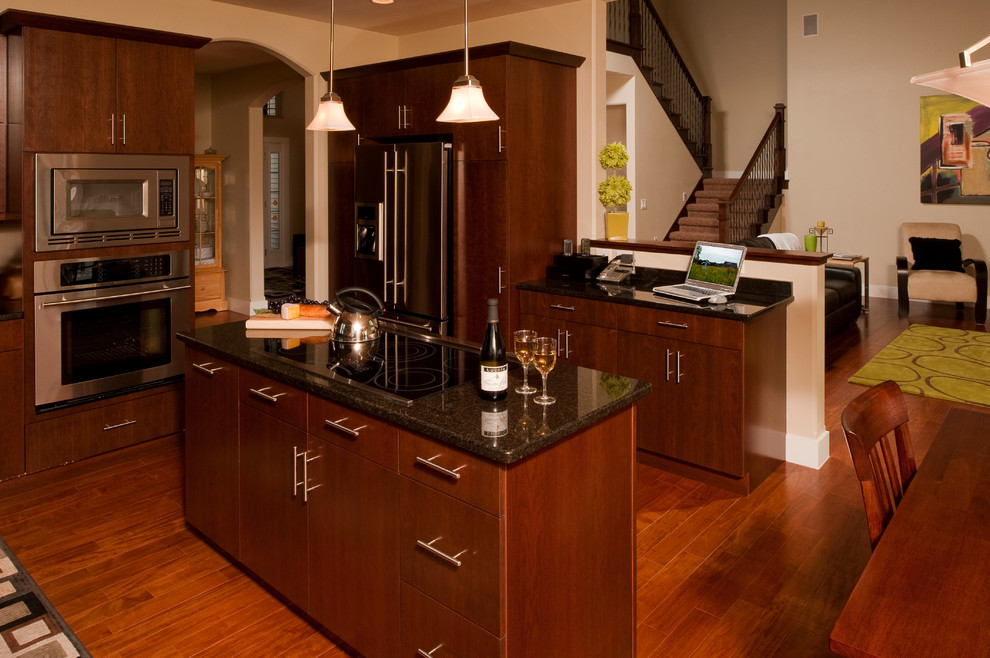 This is an example of a mid-sized modern u-shaped open plan kitchen in Cedar Rapids with an undermount sink, flat-panel cabinets, dark wood cabinets, granite benchtops, black splashback, stone slab splashback, stainless steel appliances, dark hardwood floors, with island and brown floor.