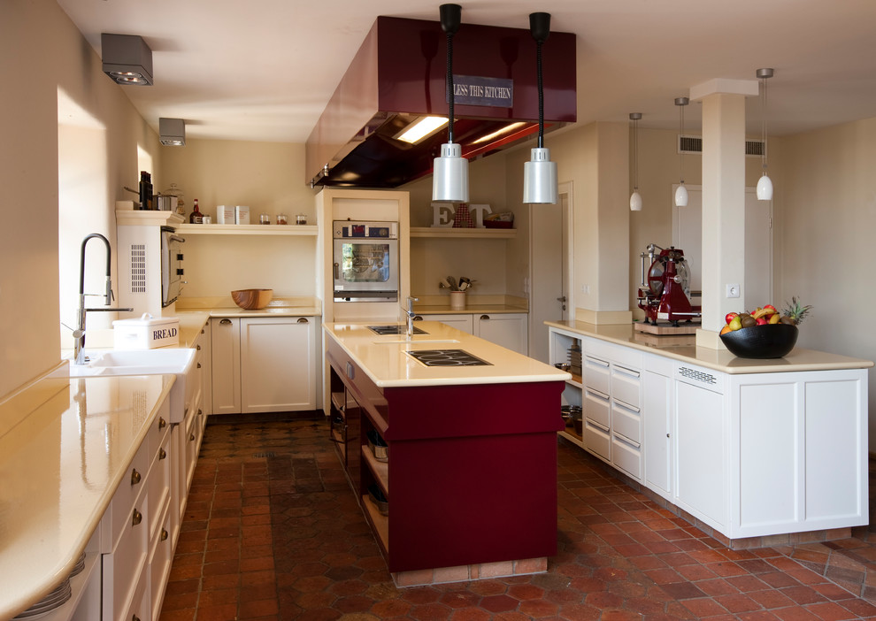 Inspiration for a mid-sized country u-shaped open plan kitchen in Berlin with a farmhouse sink, recessed-panel cabinets, white cabinets, beige splashback, stainless steel appliances, brick floors, multiple islands and red floor.