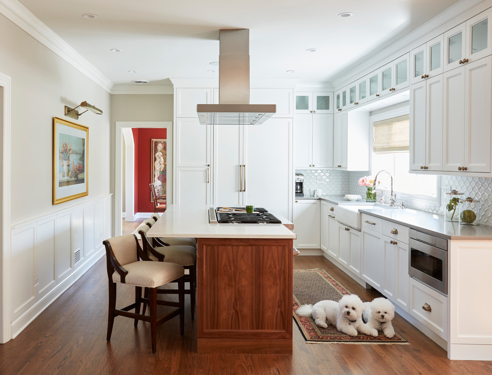 Large traditional l-shaped kitchen in Chicago with a farmhouse sink, shaker cabinets, white cabinets, quartzite benchtops, white splashback, porcelain splashback, panelled appliances, dark hardwood floors, with island and brown floor.