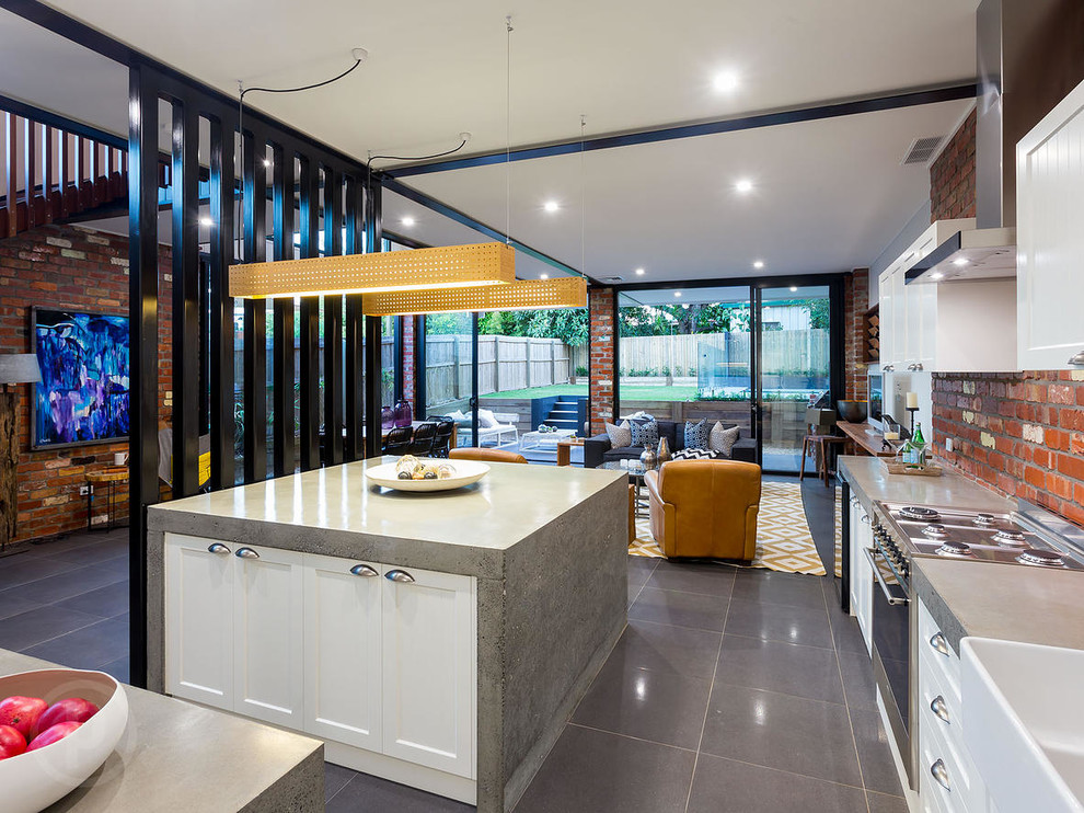 Design ideas for a large industrial l-shaped open plan kitchen in Brisbane with a farmhouse sink, beaded inset cabinets, white cabinets, concrete benchtops, red splashback, brick splashback, stainless steel appliances, ceramic floors, with island and grey floor.