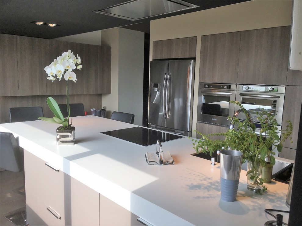 Large contemporary galley eat-in kitchen in Rennes with an undermount sink, flat-panel cabinets, medium wood cabinets, white splashback, stainless steel appliances, ceramic floors, with island, brown floor and white benchtop.