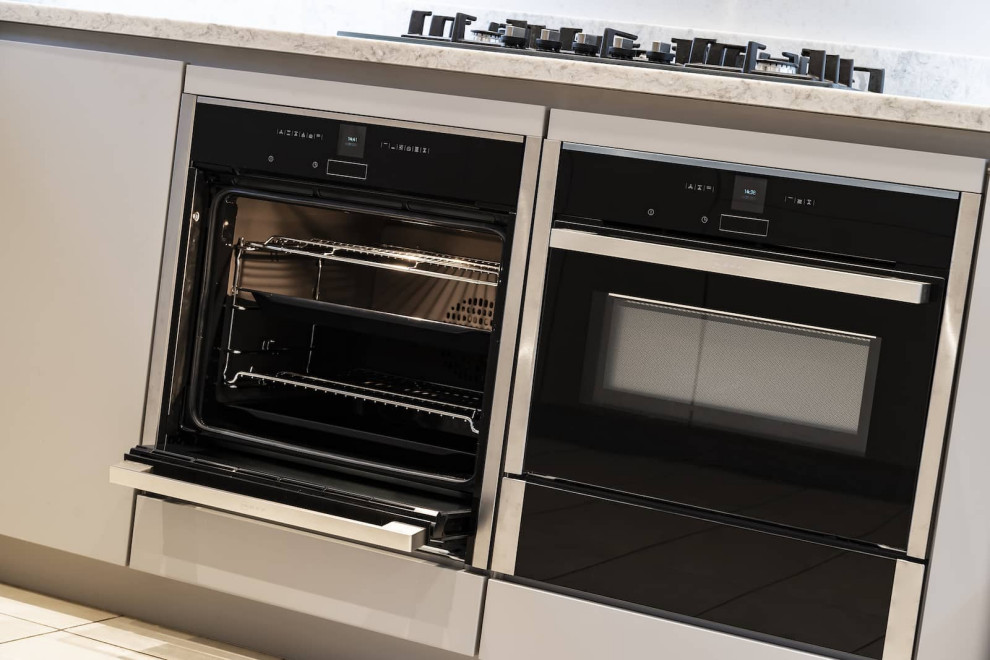 Offene, Mittelgroße Moderne Küche in U-Form mit flächenbündigen Schrankfronten, grauen Schränken und schwarzen Elektrogeräten in Oxfordshire