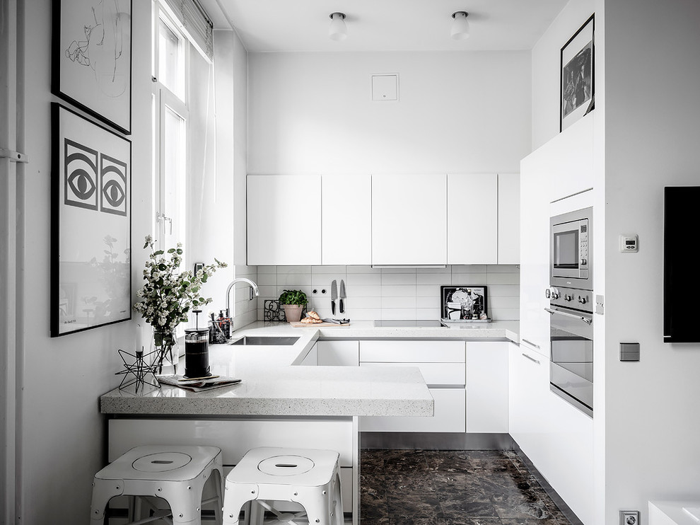 This is an example of a scandinavian u-shaped separate kitchen in Gothenburg with a single-bowl sink, flat-panel cabinets, white cabinets, white splashback, panelled appliances, a peninsula, brown floor and grey benchtop.