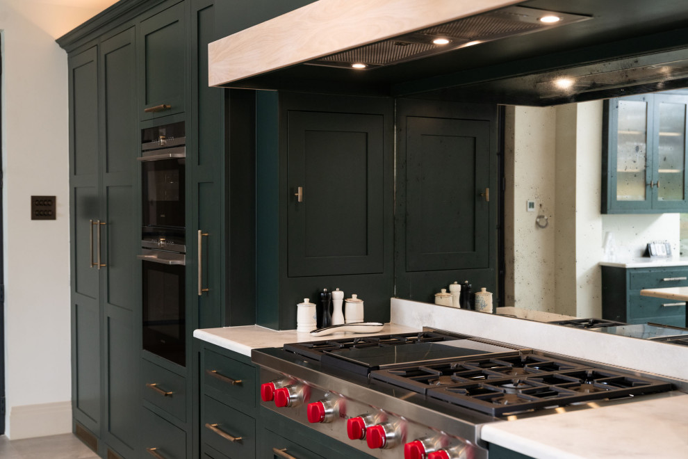 Industriell inredning av ett stort grå grått kök, med en rustik diskho, släta luckor, gröna skåp, bänkskiva i kvartsit, stänkskydd med metallisk yta, spegel som stänkskydd, rostfria vitvaror, kalkstensgolv, en köksö och grått golv