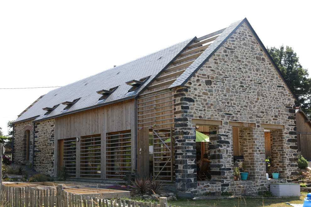 Aménagement d'une grande façade de maison grise campagne en pierre à un étage avec un toit à deux pans et un toit gris.