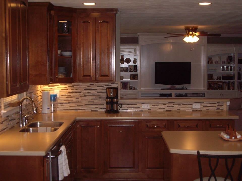 Example of a l-shaped eat-in kitchen design with a drop-in sink, recessed-panel cabinets, medium tone wood cabinets, laminate countertops, multicolored backsplash, matchstick tile backsplash, stainless steel appliances and an island