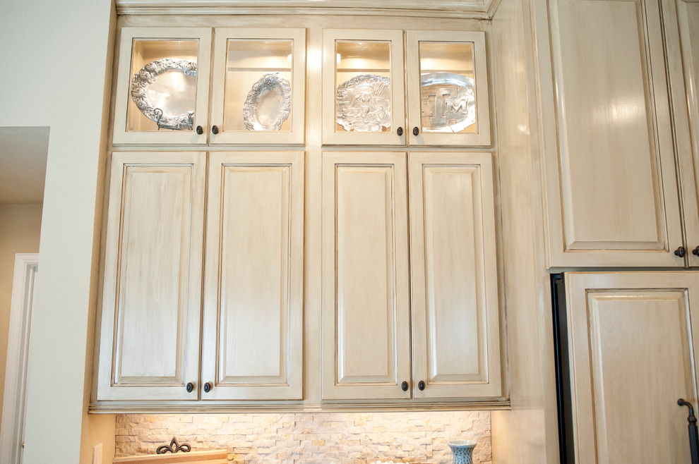This is an example of a mid-sized transitional open plan kitchen in Houston with a farmhouse sink, raised-panel cabinets, beige cabinets, granite benchtops, beige splashback, stone tile splashback, panelled appliances, travertine floors and with island.