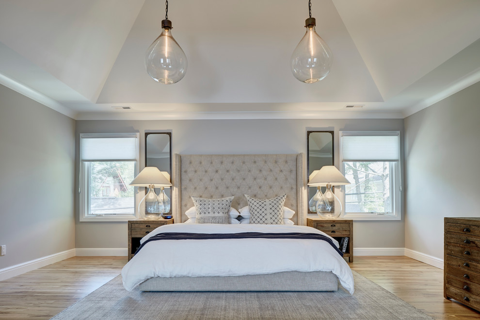 Inspiration for a large transitional master bedroom in Detroit with grey walls, a standard fireplace, a stone fireplace surround and light hardwood floors.