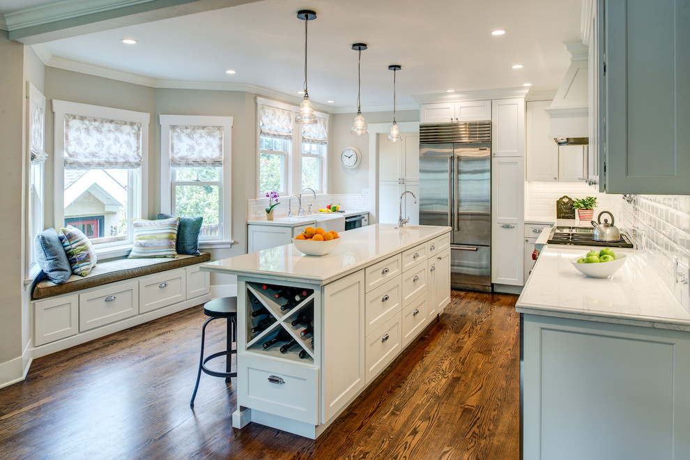 Photo of a mid-sized transitional u-shaped separate kitchen in San Francisco with a farmhouse sink, shaker cabinets, white cabinets, quartz benchtops, white splashback, subway tile splashback, stainless steel appliances, medium hardwood floors, with island and brown floor.