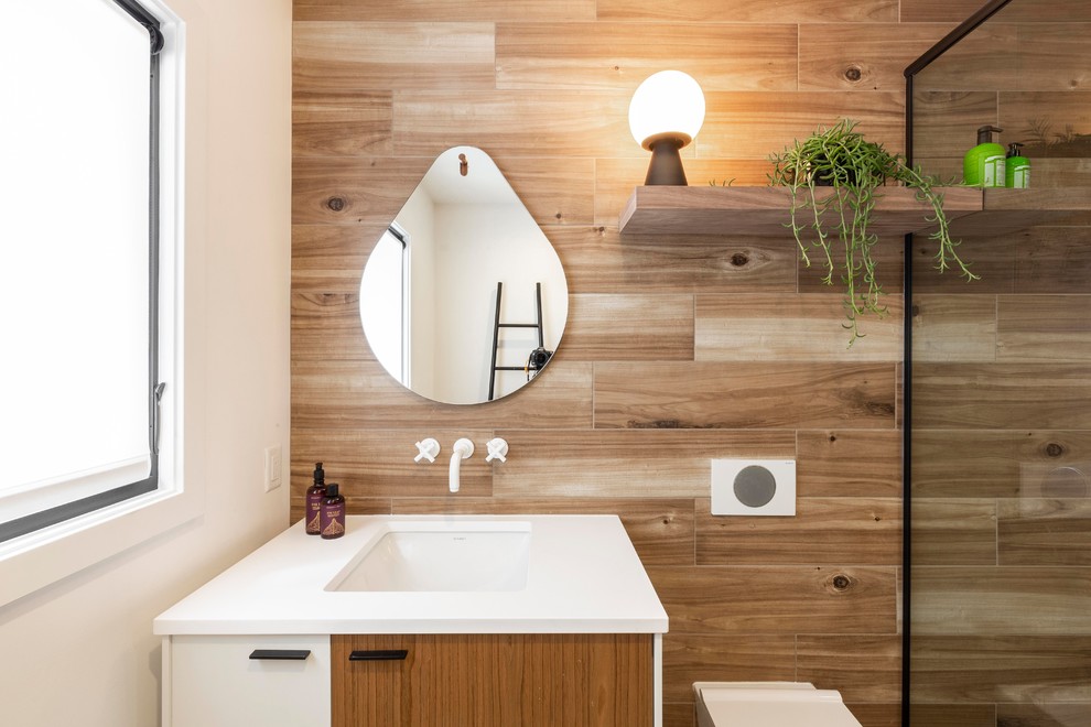 Photo of a mid-sized contemporary kids bathroom in Portland with flat-panel cabinets, medium wood cabinets, a corner shower, a wall-mount toilet, white tile, subway tile, brown walls, porcelain floors, an undermount sink, quartzite benchtops, grey floor, a hinged shower door and white benchtops.