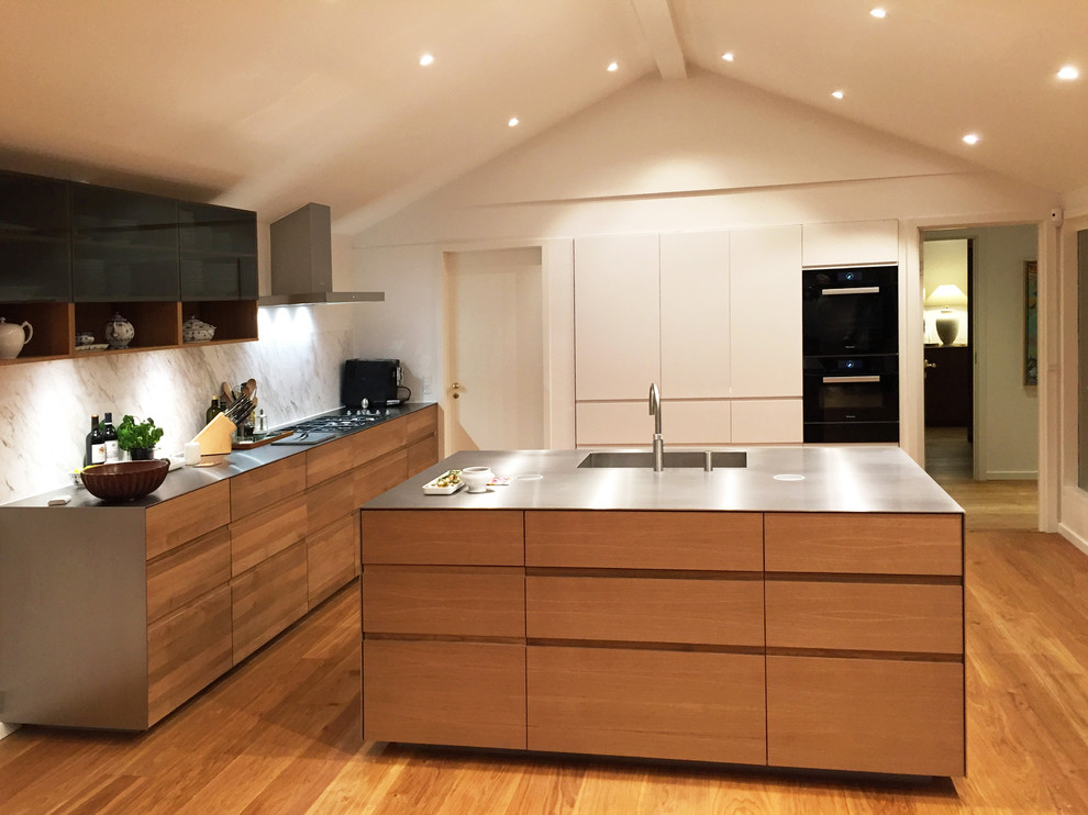 Expansive modern open plan kitchen in Copenhagen with an integrated sink, flat-panel cabinets, medium wood cabinets, stainless steel benchtops, marble splashback, panelled appliances and with island.