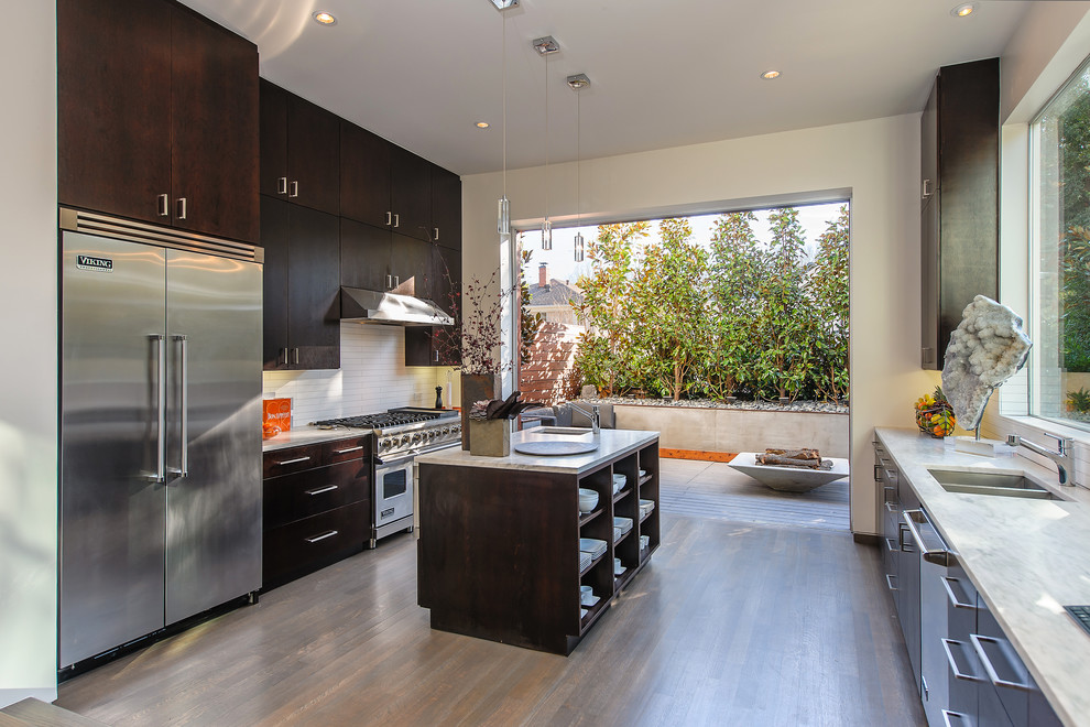 Inspiration for a large contemporary kitchen in Seattle with a double-bowl sink, flat-panel cabinets, dark wood cabinets, white splashback, stainless steel appliances, light hardwood floors and with island.