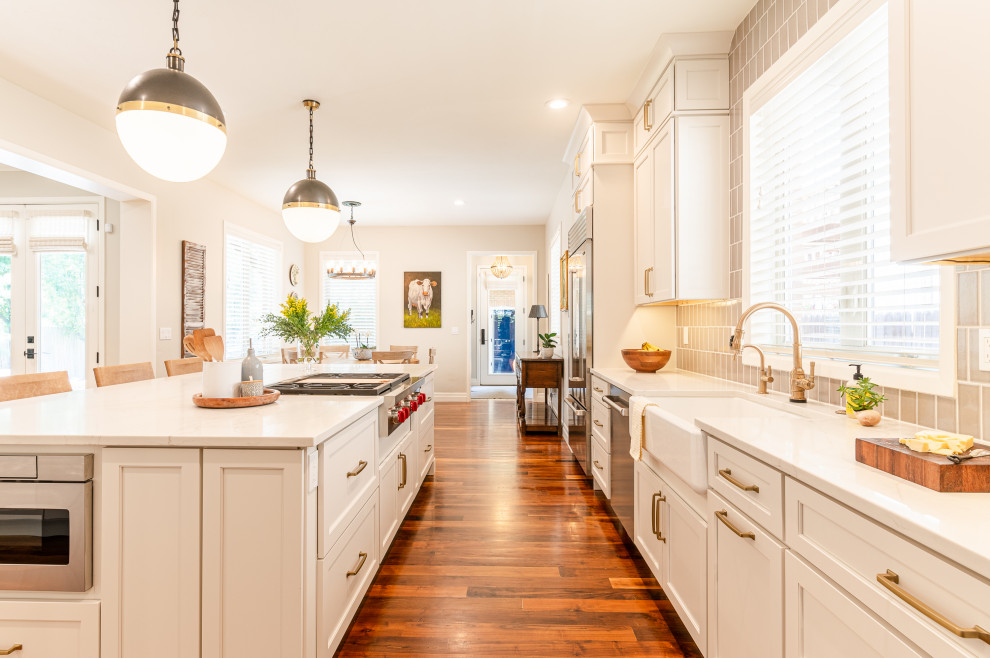 Inspiration for a large transitional l-shaped dark wood floor and brown floor open concept kitchen remodel in Denver with a farmhouse sink, shaker cabinets, beige cabinets, quartz countertops, beige backsplash, ceramic backsplash, stainless steel appliances, an island and white countertops