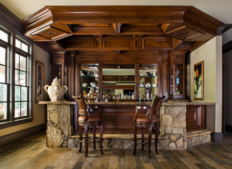Large traditional u-shaped seated home bar in Atlanta with an undermount sink, recessed-panel cabinets, dark wood cabinets, granite benchtops, porcelain floors, brown splashback, brown floor, mirror splashback and multi-coloured benchtop.