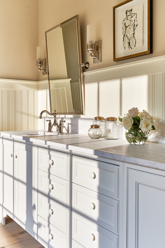 Large traditional master bathroom in Charlotte with raised-panel cabinets, white cabinets, a one-piece toilet, gray tile, stone slab, beige walls, light hardwood floors, a drop-in sink and solid surface benchtops.