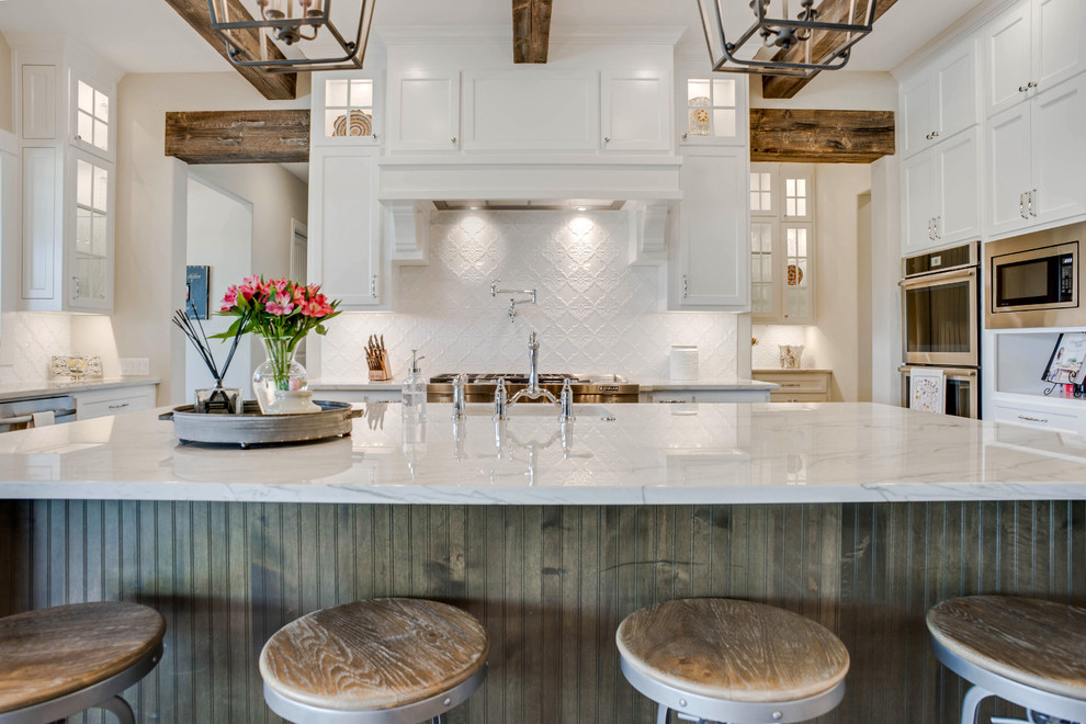 This is an example of a large traditional u-shaped open plan kitchen in Dallas with a farmhouse sink, shaker cabinets, brown cabinets, quartzite benchtops, white splashback, ceramic splashback, stainless steel appliances, medium hardwood floors, with island, brown floor and white benchtop.