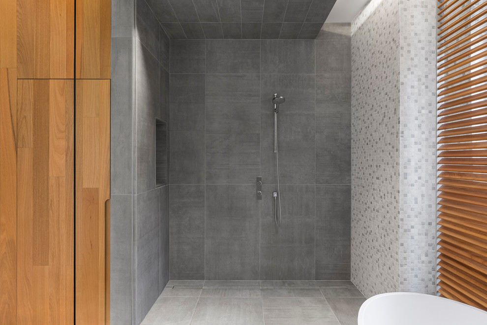Mid-sized contemporary master bathroom in Montreal with flat-panel cabinets, light wood cabinets, a freestanding tub, an open shower, gray tile, grey walls, ceramic floors and an integrated sink.