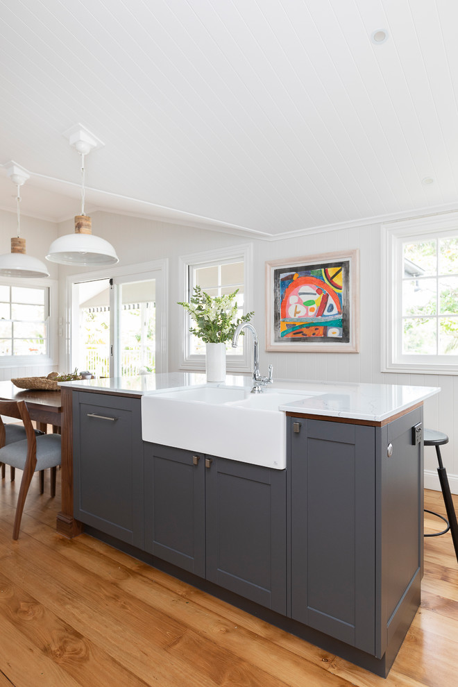 This is an example of a transitional eat-in kitchen in Brisbane with a farmhouse sink, recessed-panel cabinets, grey cabinets, medium hardwood floors and white benchtop.