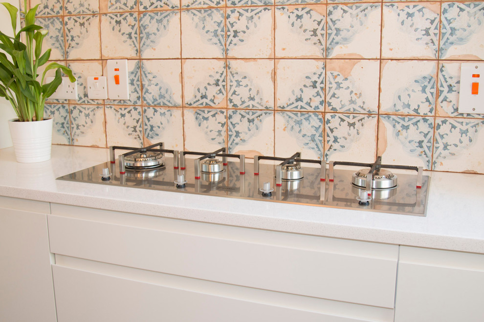 Photo of a small eclectic l-shaped open plan kitchen with a built-in sink, flat-panel cabinets, beige cabinets, quartz worktops, beige splashback, cement tile splashback, stainless steel appliances, laminate floors, an island and brown floors.
