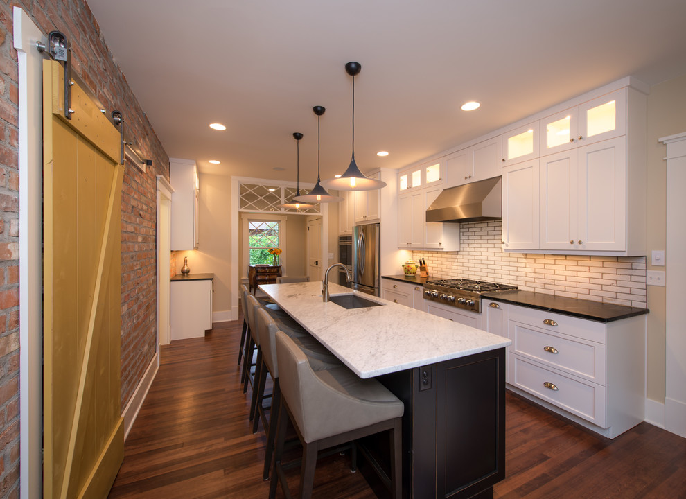 Photo of a transitional galley kitchen in Denver with an undermount sink, shaker cabinets, white cabinets, white splashback, subway tile splashback, stainless steel appliances, dark hardwood floors and with island.