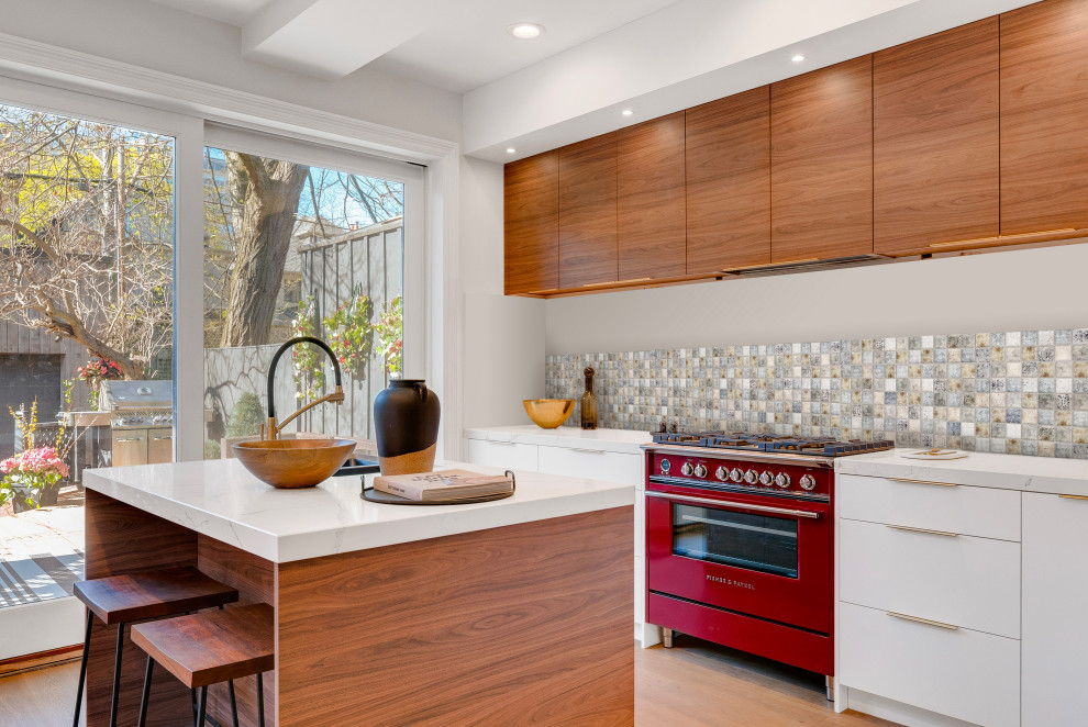 This is an example of a contemporary kitchen in Paris with flat-panel cabinets, white cabinets, multi-coloured splashback, mosaic tile splashback, coloured appliances, light hardwood floors, with island, beige floor and white benchtop.
