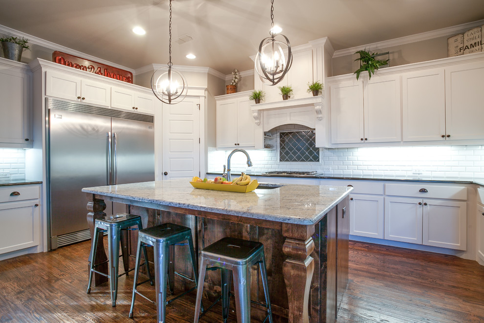 Photo of a large country u-shaped open plan kitchen in Dallas with an undermount sink, shaker cabinets, white cabinets, granite benchtops, white splashback, subway tile splashback, stainless steel appliances, medium hardwood floors and with island.