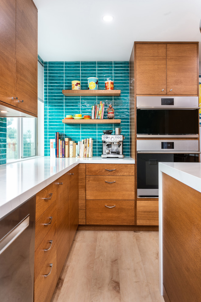 Small midcentury galley eat-in kitchen in Los Angeles with an undermount sink, flat-panel cabinets, medium wood cabinets, quartz benchtops, blue splashback, stainless steel appliances, laminate floors, with island and white benchtop.