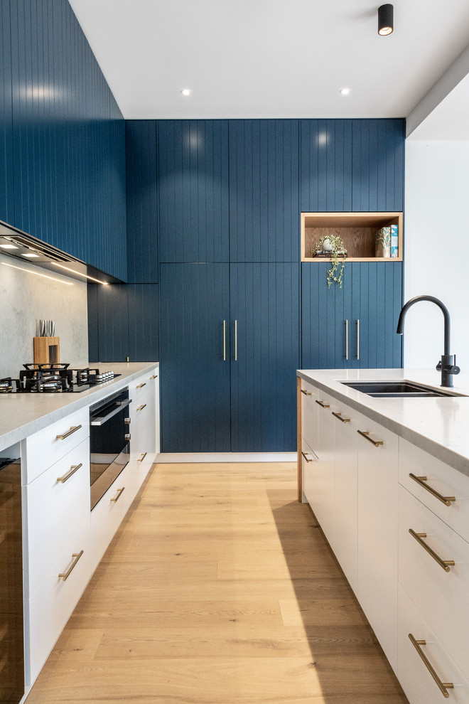 Photo of a contemporary galley kitchen in Sydney with an undermount sink, quartz benchtops, marble splashback, black appliances, light hardwood floors, multiple islands and multi-coloured benchtop.