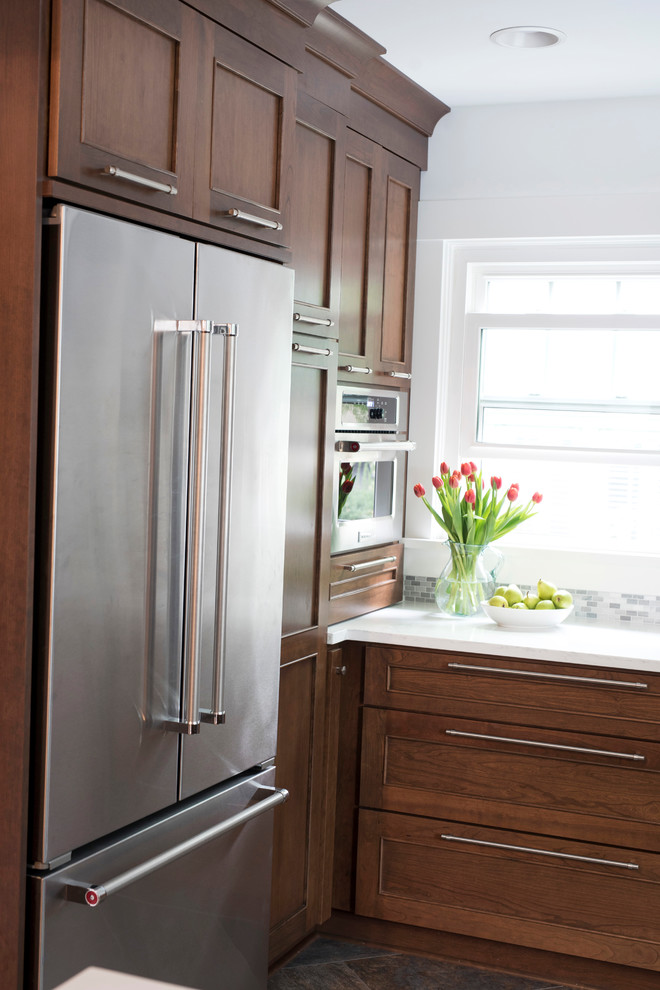 Mid-sized transitional u-shaped vinyl floor and multicolored floor kitchen photo with an undermount sink, shaker cabinets, brown cabinets, quartz countertops, gray backsplash, marble backsplash, stainless steel appliances, no island and white countertops
