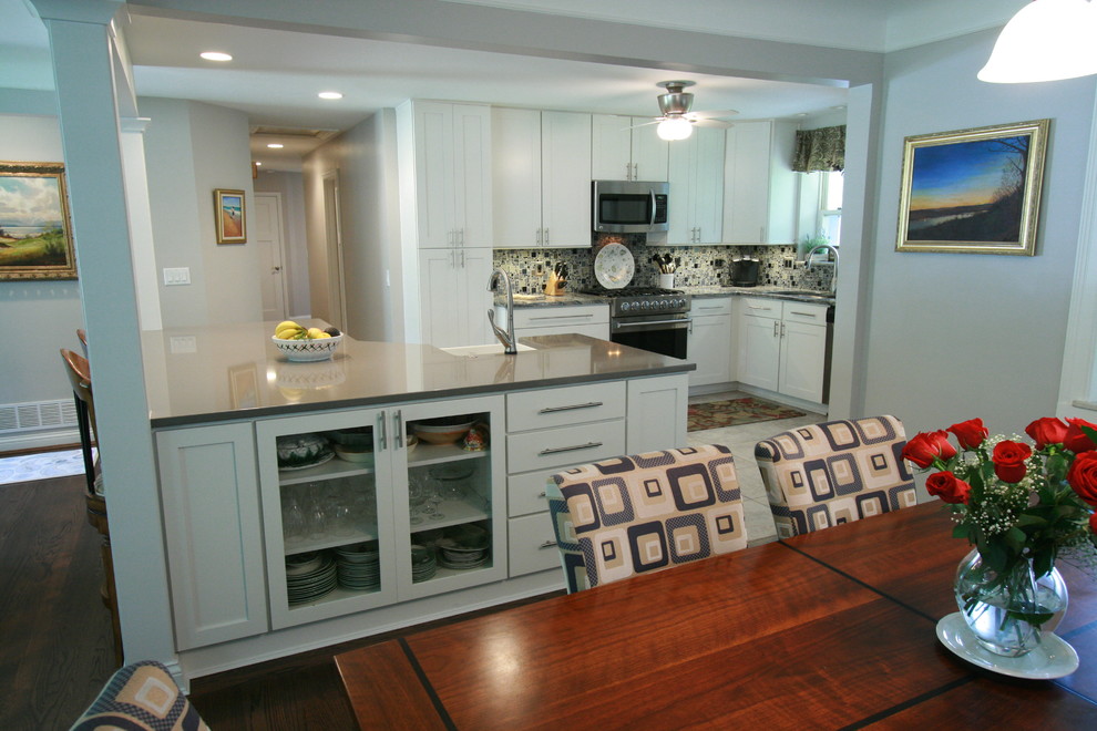 Mid-sized transitional dark wood floor eat-in kitchen photo in Cincinnati with a farmhouse sink, flat-panel cabinets, white cabinets, quartz countertops, multicolored backsplash, ceramic backsplash, stainless steel appliances and an island