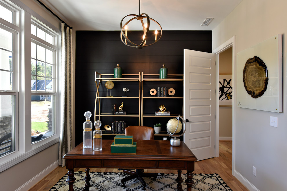 This is an example of a transitional home office in DC Metro with black walls, light hardwood floors and a freestanding desk.