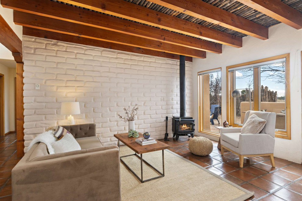 Inspiration for a small open concept living room in Other with white walls, terra-cotta floors, a wood stove, a brick fireplace surround, no tv, brown floor, exposed beam and brick walls.
