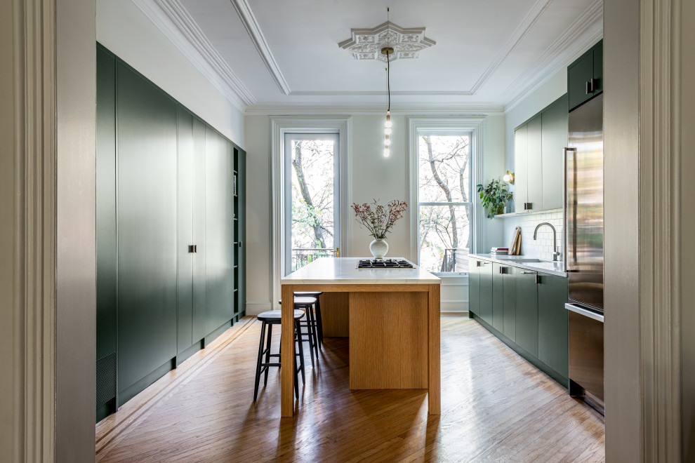 Design ideas for an eat-in kitchen in New York with a single-bowl sink, flat-panel cabinets, green cabinets, quartz benchtops, white splashback, engineered quartz splashback, stainless steel appliances, light hardwood floors, with island and white benchtop.