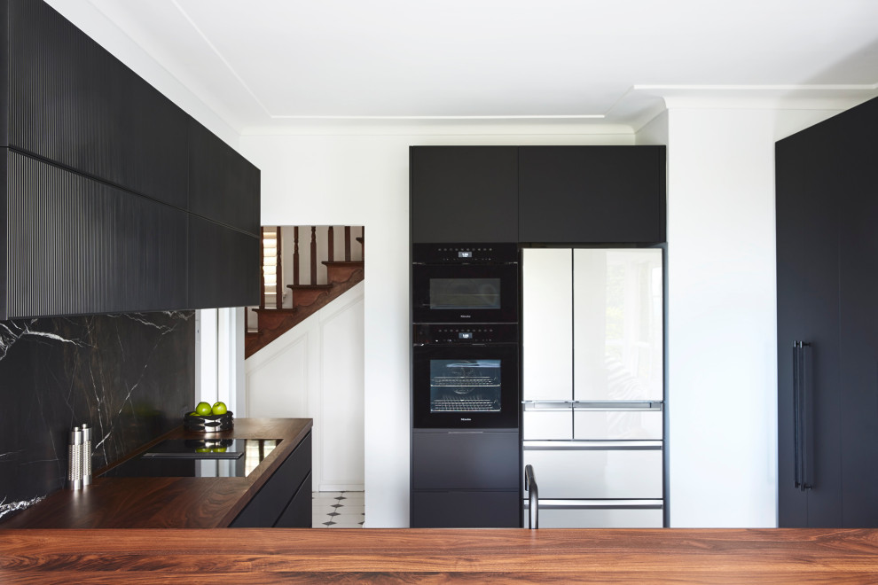 Example of a mid-sized trendy l-shaped porcelain tile and gray floor enclosed kitchen design in Sydney with a single-bowl sink, flat-panel cabinets, black cabinets, wood countertops, black backsplash, marble backsplash, black appliances, no island and brown countertops