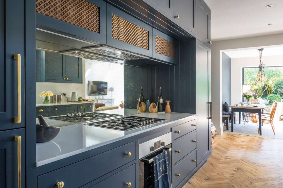 This is an example of a mid-sized traditional galley eat-in kitchen in London with a farmhouse sink, shaker cabinets, blue cabinets, mirror splashback, stainless steel appliances, no island and white benchtop.