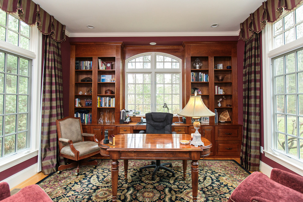 Design ideas for a mid-sized traditional home office in Boston with a library, red walls, medium hardwood floors, a freestanding desk and multi-coloured floor.