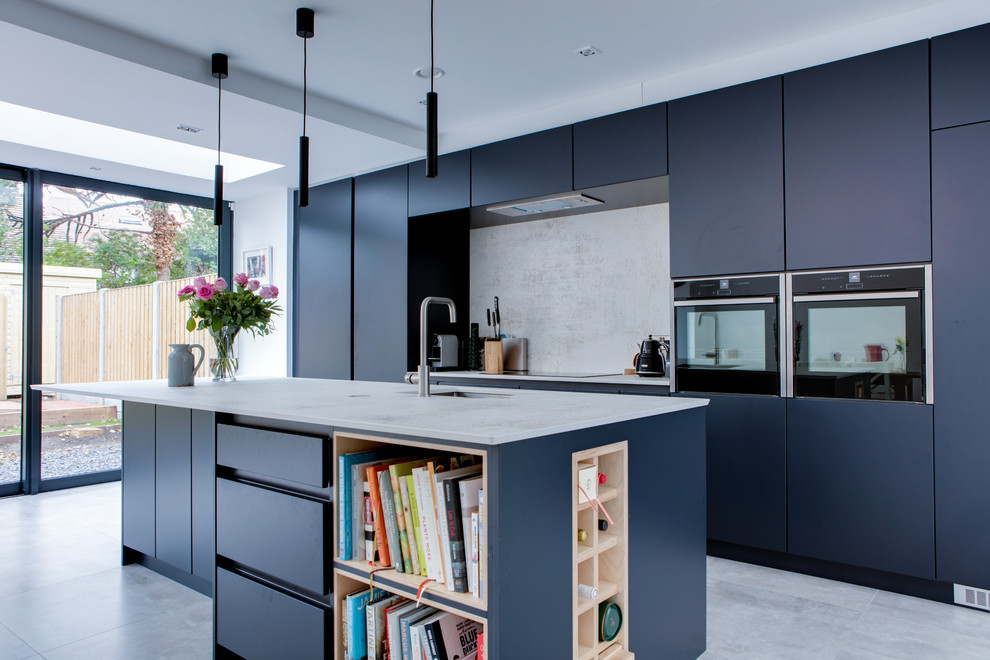 Mid-sized contemporary galley open plan kitchen in Dublin with a drop-in sink, flat-panel cabinets, blue cabinets, quartzite benchtops, grey splashback, stone slab splashback, stainless steel appliances, porcelain floors, with island, grey floor and grey benchtop.