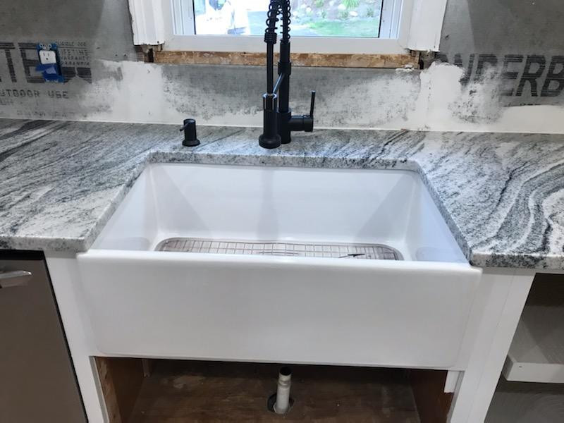 Mid-sized l-shaped open concept kitchen photo with a farmhouse sink, white cabinets, granite countertops, stainless steel appliances, a peninsula and gray countertops