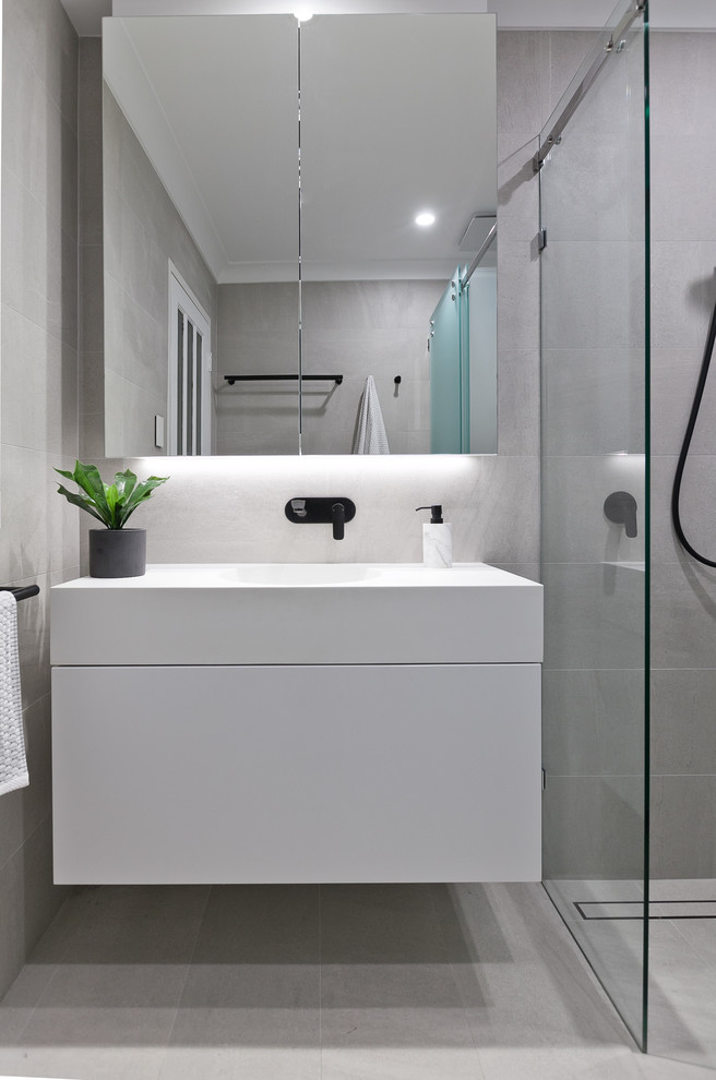 Photo of a small contemporary 3/4 bathroom in Perth with flat-panel cabinets, white cabinets, a two-piece toilet, beige tile, porcelain tile, beige walls, porcelain floors, an integrated sink, solid surface benchtops, beige floor, a sliding shower screen and white benchtops.