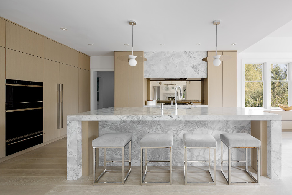 Design ideas for an expansive contemporary l-shaped open plan kitchen in New York with a submerged sink, flat-panel cabinets, beige cabinets, marble worktops, mirror splashback, integrated appliances, light hardwood flooring, an island, beige floors and grey worktops.